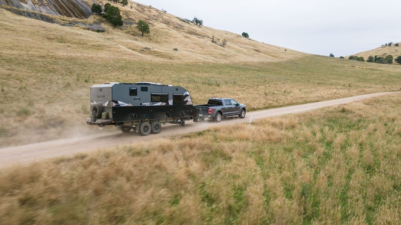 A caravan being towed along a gravel road through the hills